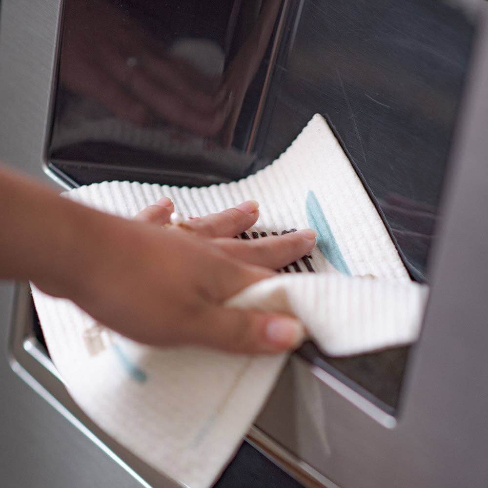 Person using Swedish dishcloth to clean refrigerator surface, showcasing eco-friendly cleaning product.
