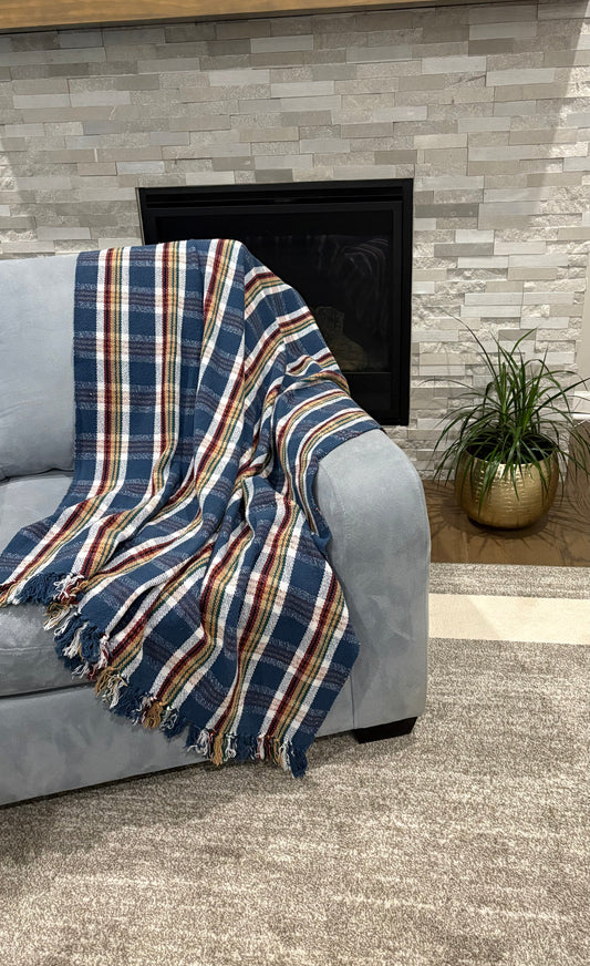 Plaid blanket draped over a gray sofa in front of a stone fireplace.