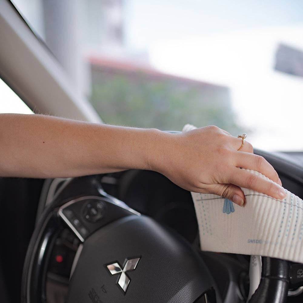 Woman using eco-friendly Swedish dishcloth to clean steering wheel in car.