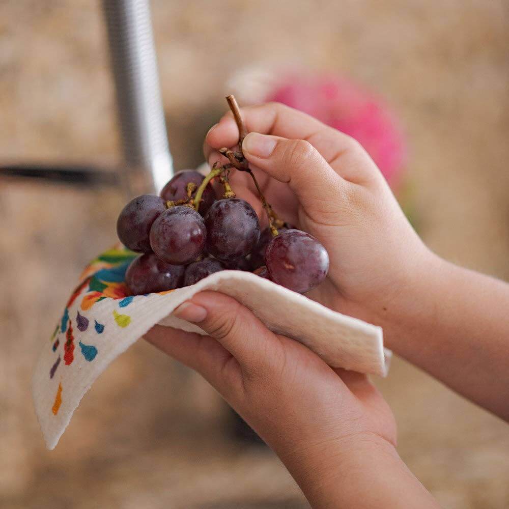 Hands holding grapes on a Swedish dishcloth featuring a colorful fruit design, eco-friendly and reusable.