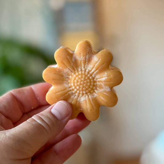 Hand holding a yellow flower-shaped honey turmeric tallow face bar soap, showcasing its unique design and color.