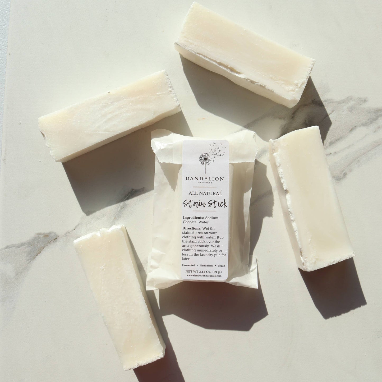 All-natural laundry stain stick surrounded by pieces of soap on a marble surface, ideal for sensitive skin.