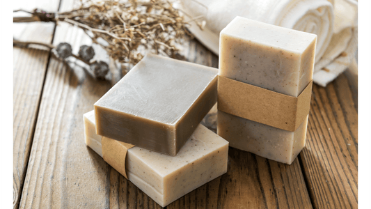 Three natural soap bars with dried herbs and a towel in the background.
