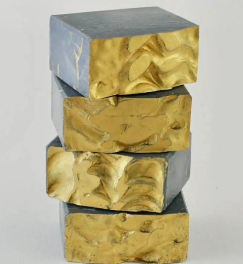 Four organic, black gold soap bars stacked on top of each other.