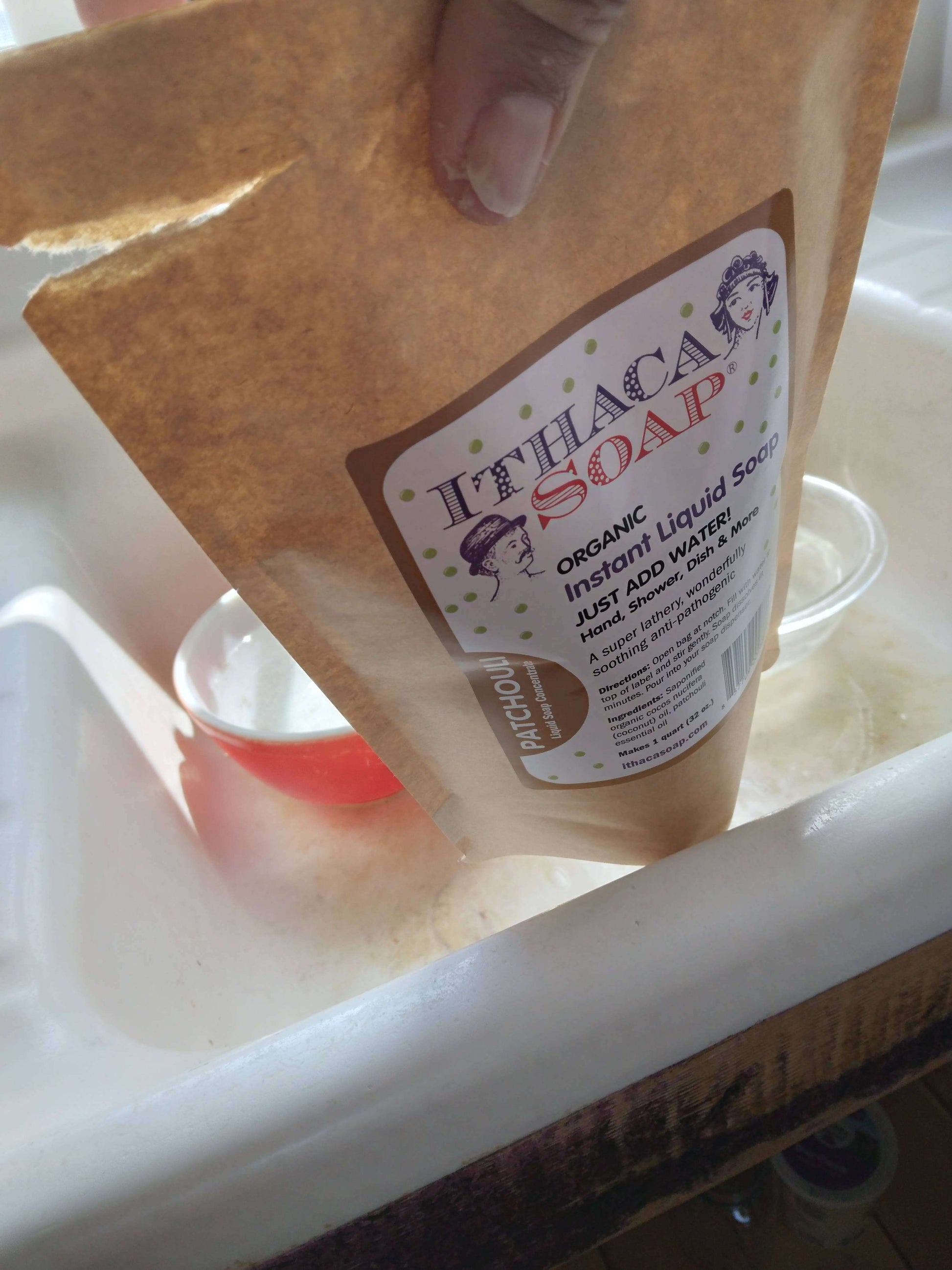 Hand pouring organic instant liquid soap refill into sink for easy mixing with water.