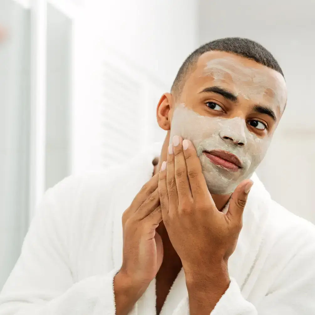 Man applying a Bentonite clay face mask in a bathroom, promoting skincare and deep pore cleansing.