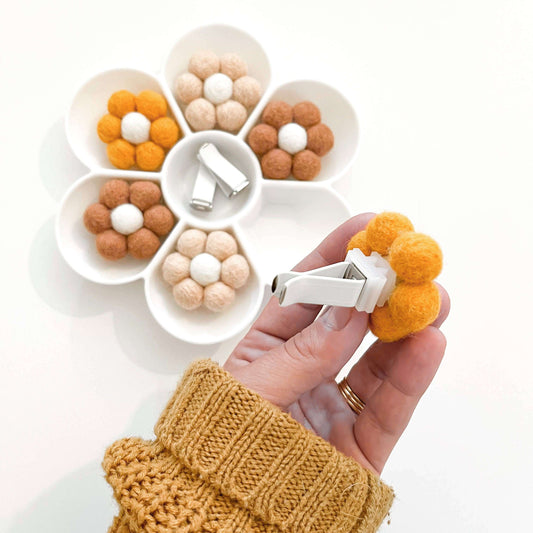 Yellow daisy car vent clip essential oil diffuser held by a hand, surrounded by felt flower decor in a bowl.