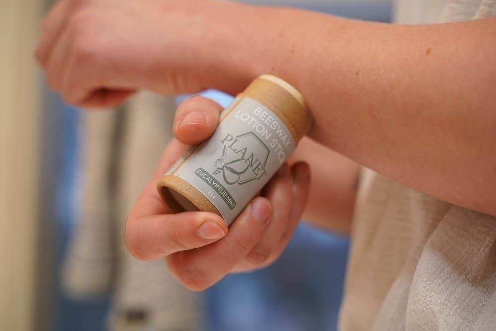 Person applying Beeswax Lotion Stick - Eucalyptus Mint from a kraft paper tube on their arm.