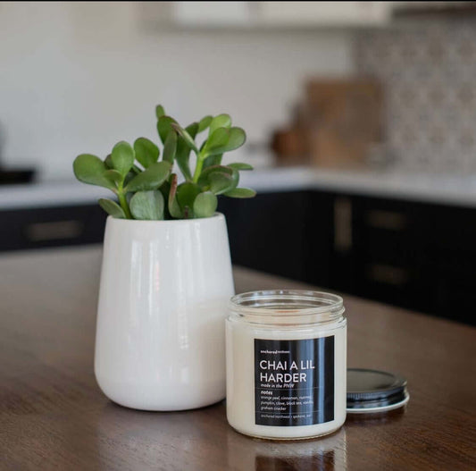 clear glass, soy candle in chai a lil harder scent sitting on counter next to a plant in a white vase