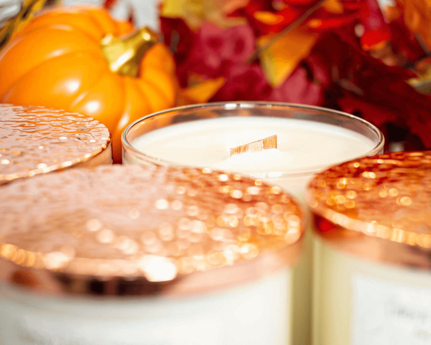 Soy wood wick candles with copper lids on, except for one, and fall leaves in the background.