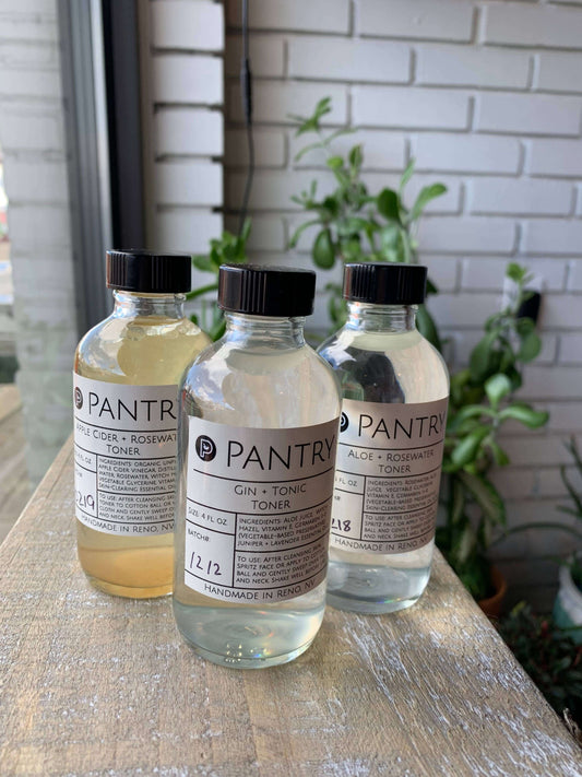 Three bottles of natural skin toners: Apple Cider Rosewater, Gin + Tonic, and Aloe + Rosewater, displayed on a wooden surface.