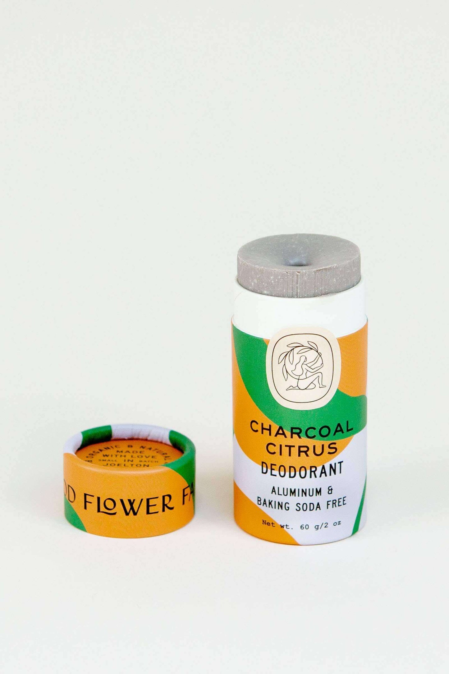 Charcoal citrus deodorant stick in a white, green and orange biodegradable tube with the lid off and sitting next to it.