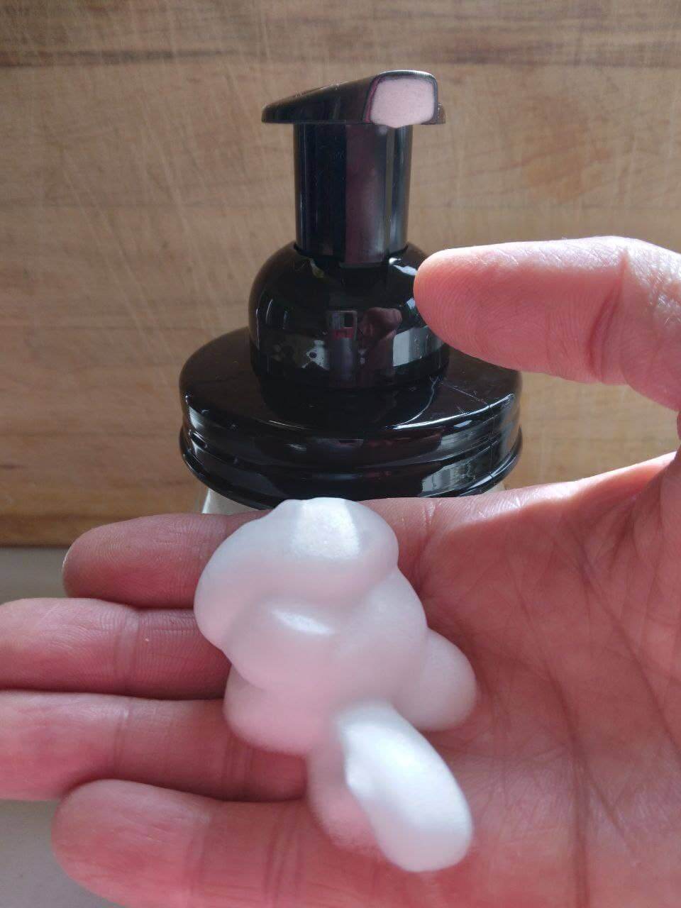 Foamy instant liquid soap squeezed into a hand from a black pump bottle.