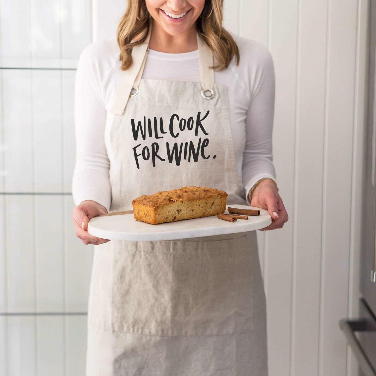 Cook for Wine Apron: Natural - Cotton Linen Blend worn by a woman holding fresh baked bread.