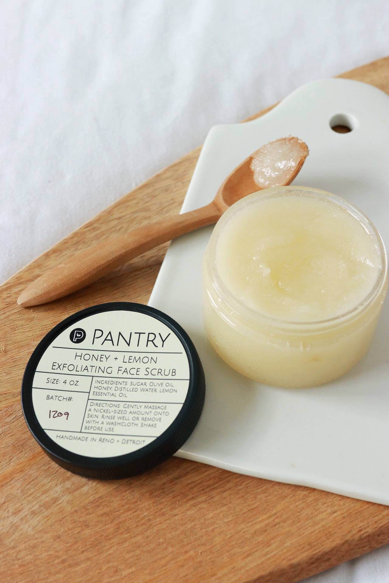 Honey and lemon exfoliating face scrub in jar with wooden spoon, perfect for winter skin brightening.