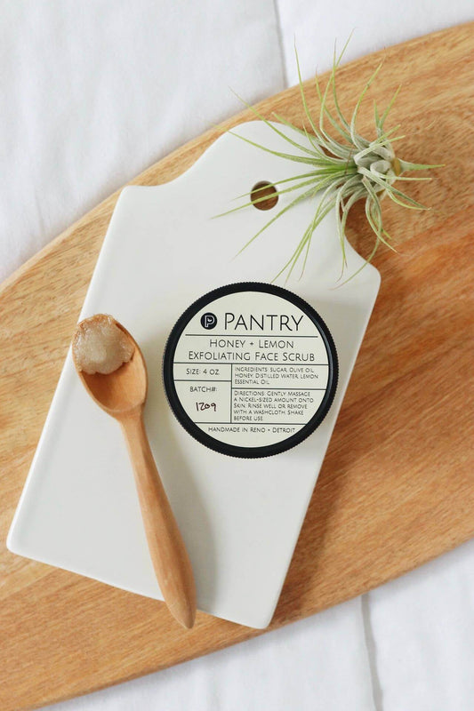 Honey + Lemon Exfoliating Face Scrub in a jar on a cutting board with a wooden spoon, perfect for brightening winter skin.