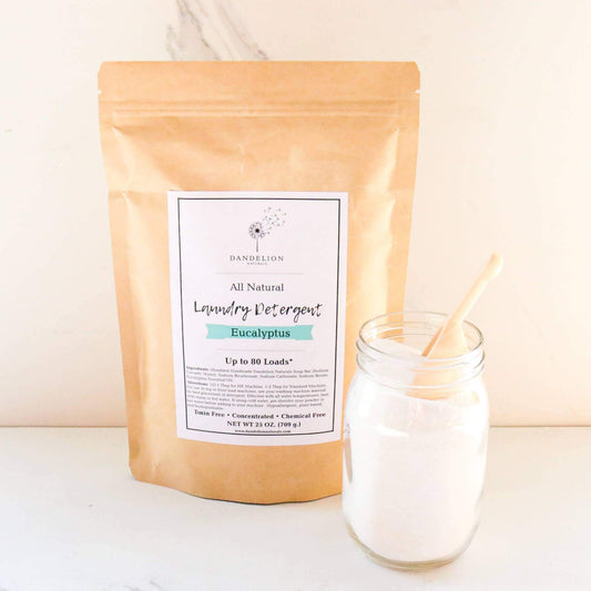 Natural laundry detergent in eucalyptus scent in a resealable brown bag and a clear glass jar filled with powder laundry detergent and a wooden spoon.