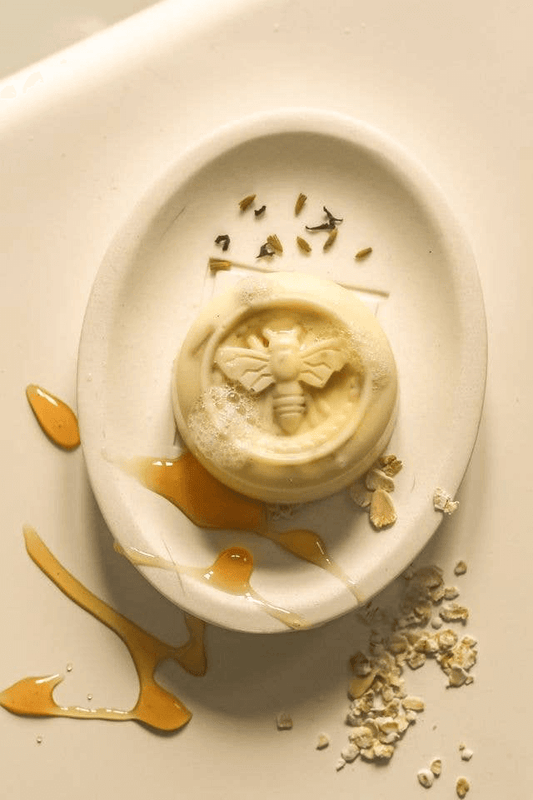 milk and honey soap with a bee design, on top of a soap dish drizzled with honey and oats