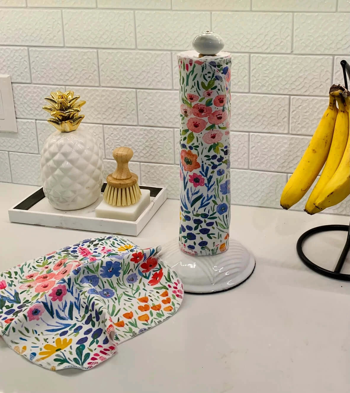 nonpaper towels with flower design on a paper towel holder, sitting next to bananas and a soap dish 