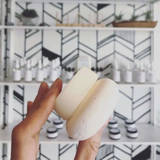 a hand holding up a shampoo and conditioner bar with a geometric wall in the background with products on shelves