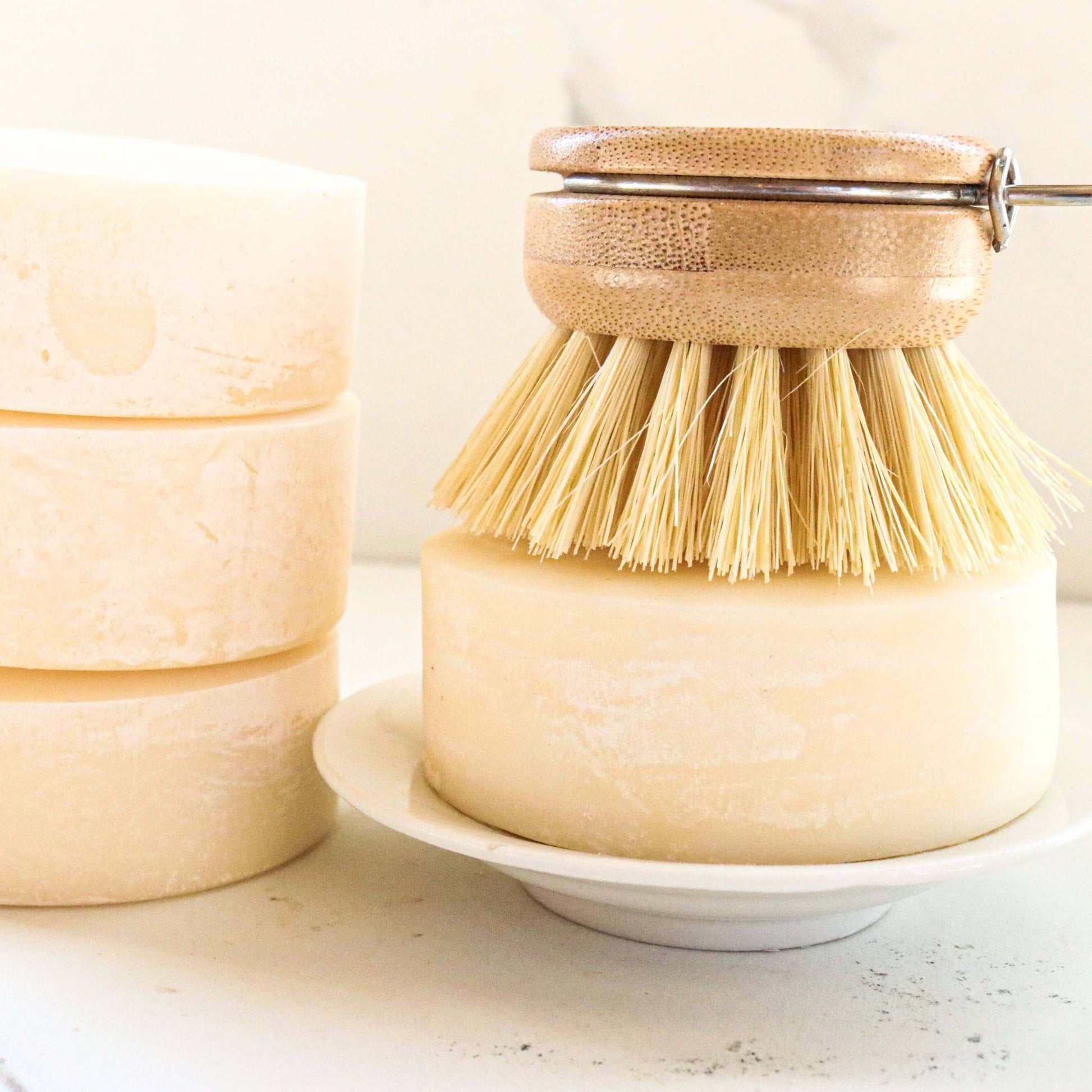 Solid dish soap bar with bamboo dish brush on a white plate, eco-friendly cleaning solution.