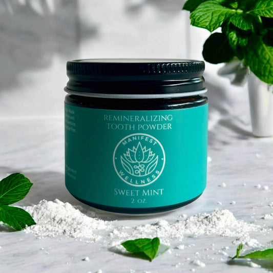 Sweet Mint Remineralizing Tooth Powder in a jar on a marble surface with mint leaves and tooth powder scattered.