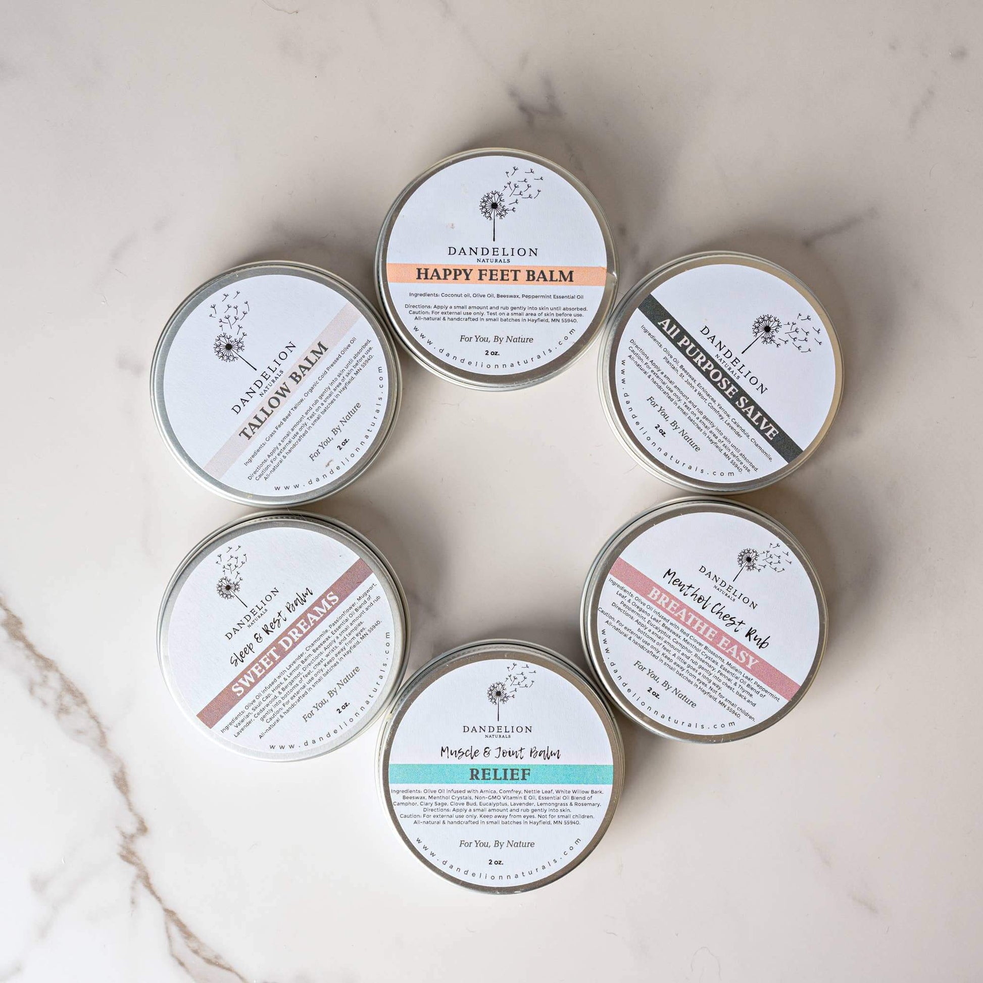Collection of Dandelion Tallow and specialty balms in circular arrangement on a marble surface.